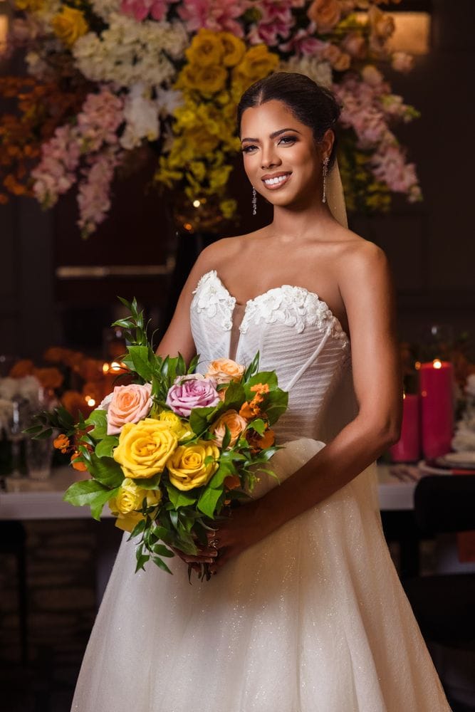 Luxury bride holding a colorful bouquet in front of an elegant floral backdrop